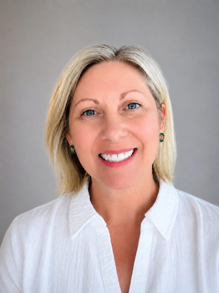 Friendly woman with a warm smile wearing a white blouse, representing care and community.