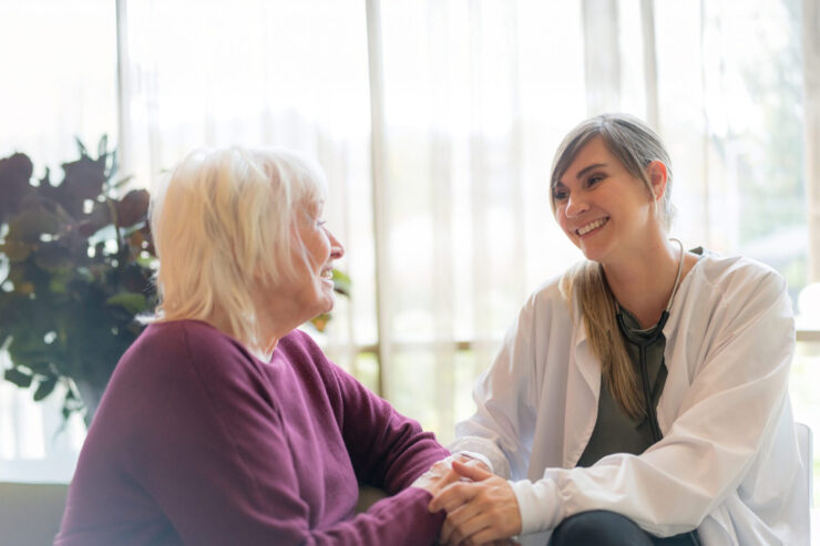 A caring healthcare professional warmly engaging with a senior woman in a sunlit room.