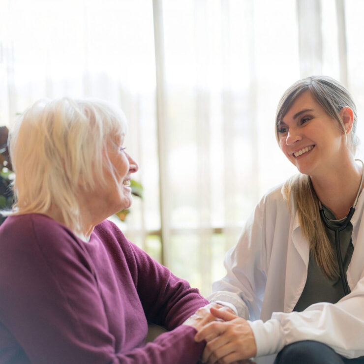 A caring healthcare professional warmly engaging with a senior woman in a sunlit room.
