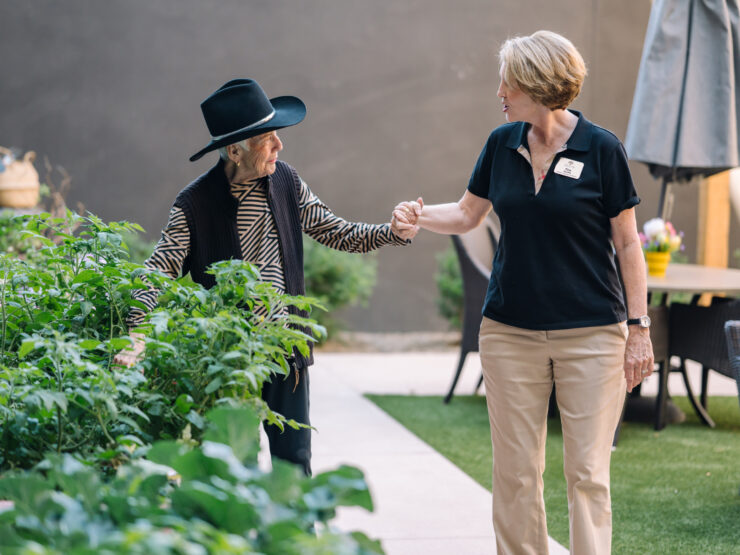 Staff member warmly assisting a senior woman in a vibrant garden area at the community center.