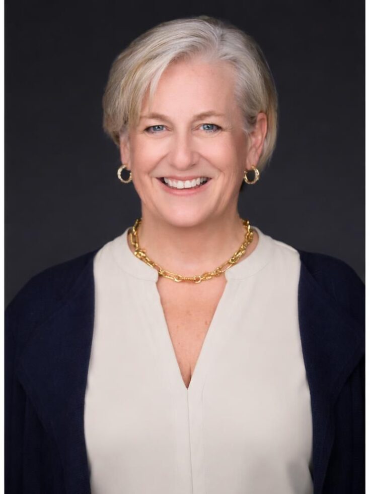 Friendly and approachable professional woman smiling warmly against a dark background.