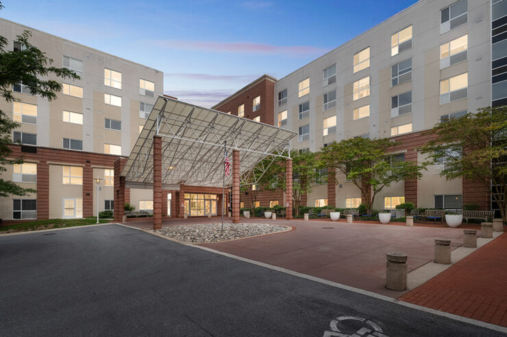 Welcoming entrance of a retirement community with well-lit windows and inviting outdoor seating.