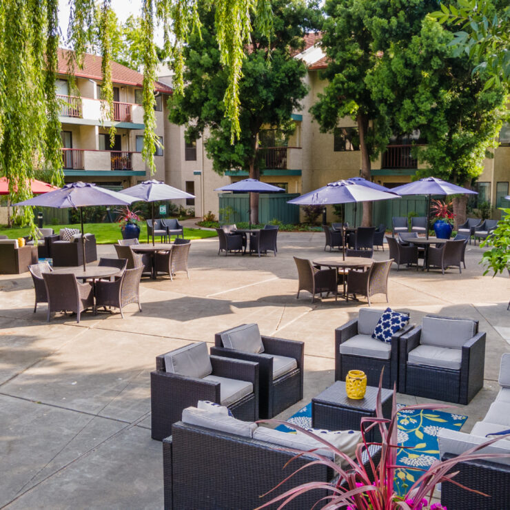 Outdoor courtyard with shaded seating areas surrounded by lush greenery and residential balconies