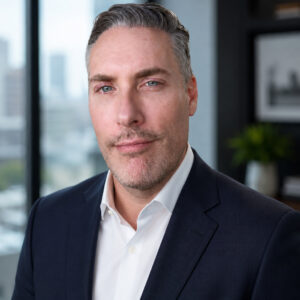 A professional man in a suit with a calm expression in a modern, light-filled office setting.