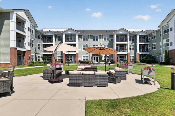 Outdoor seating area with umbrellas and greenery, surrounded by a welcoming apartment community.