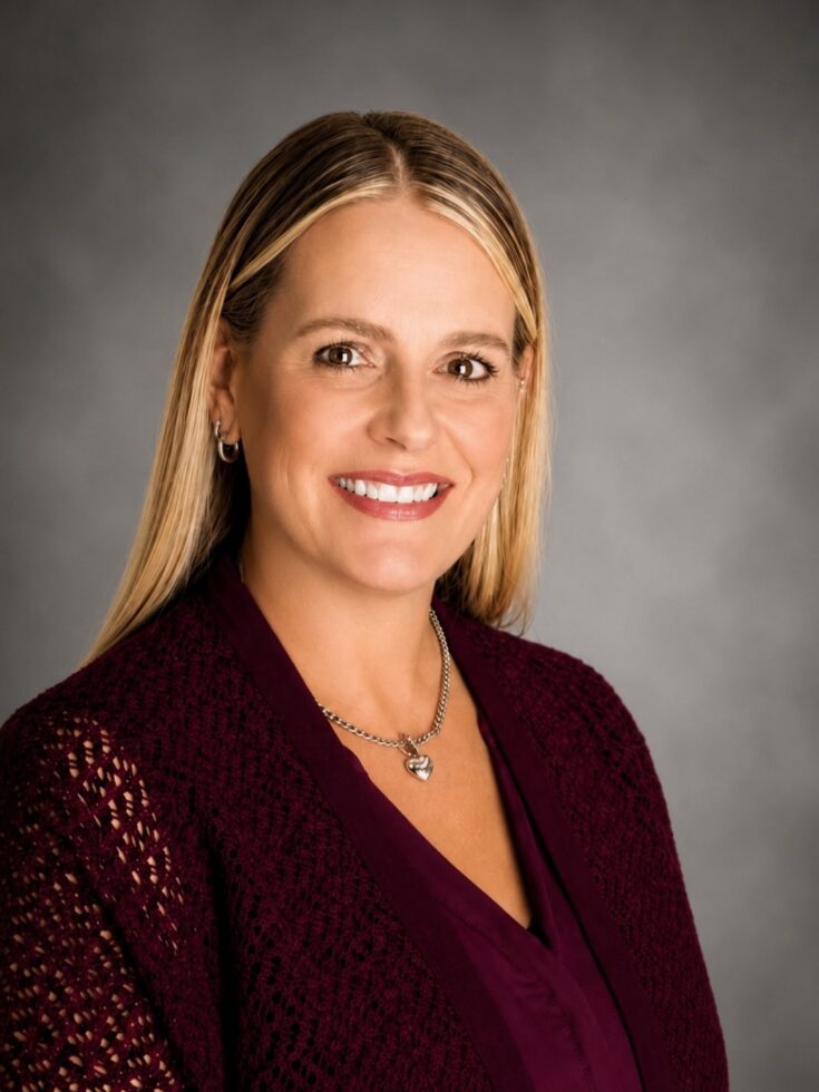Smiling woman with blonde hair wearing a warm burgundy sweater, radiating welcoming professionalism.