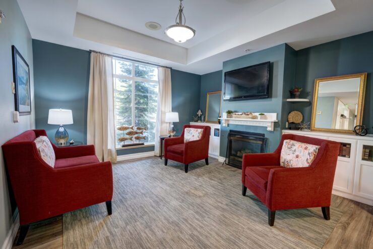 Bright common area with comfortable red armchairs, fireplace, and large window creating a welcoming space.
