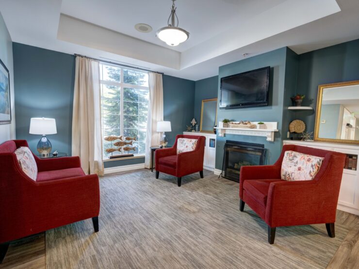 Bright common area with comfortable red armchairs, fireplace, and large window creating a welcoming space.