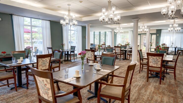 Bright, welcoming dining room with elegant chandeliers and neatly set tables for residents.