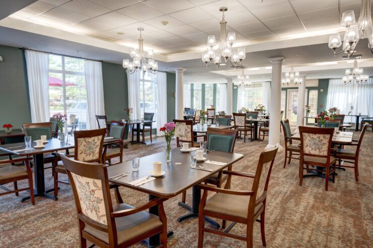 Bright, welcoming dining room with elegant chandeliers and neatly set tables for residents.