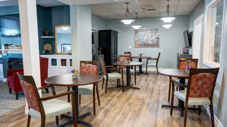Dining area with small round tables, comfortable chairs, and floral centerpieces in a warm setting.