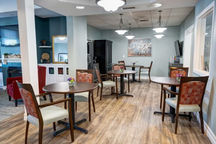 Dining area with small round tables, comfortable chairs, and floral centerpieces in a warm setting.