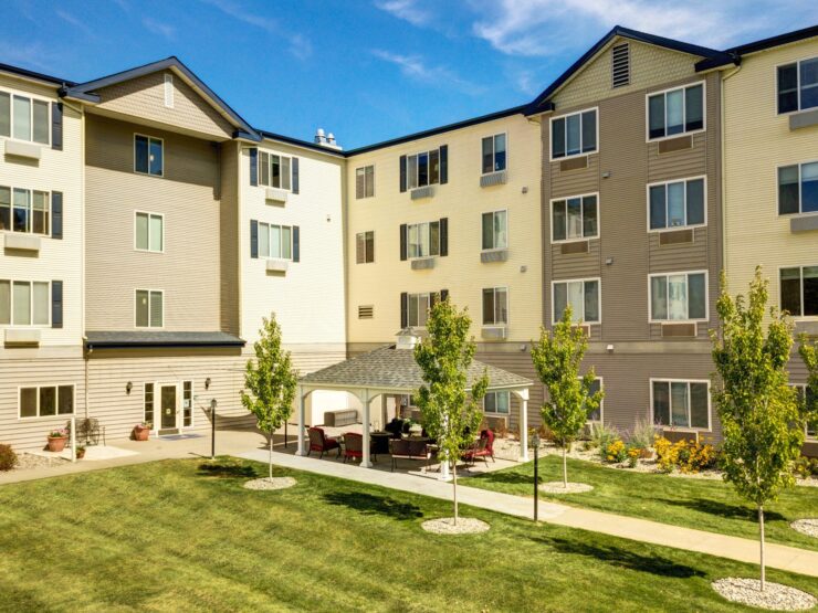Well-maintained retirement community exterior with shaded seating and green spaces for relaxation.