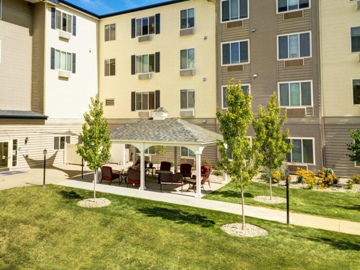 Sunny outdoor seating area with greenery beside a modern, welcoming retirement home building.