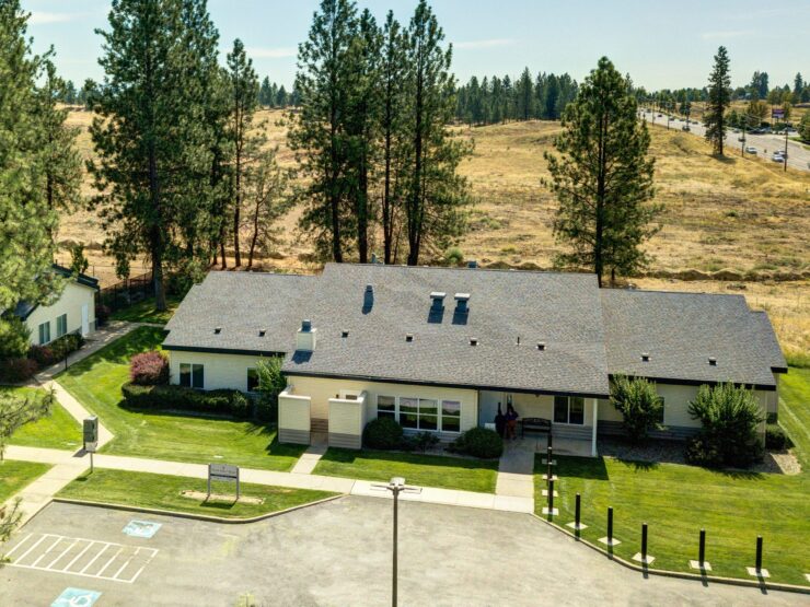 Retirement home surrounded by tall trees with people chatting near the entrance in bright weather.