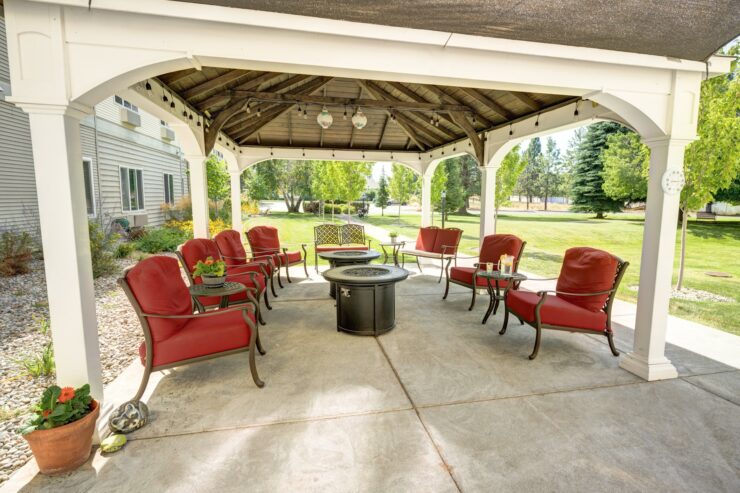 Shaded outdoor seating area with red cushioned chairs, fire pits, and garden views for relaxation and gatherings.