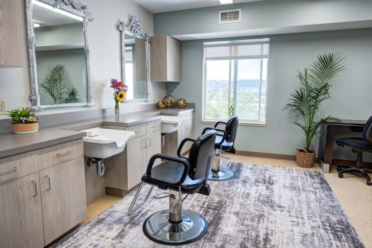 Bright salon area with styling chairs, large mirrors, plants, and natural light for residents' comfort.