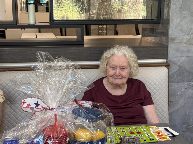 Elderly woman smiles while sitting in a bright, welcoming room with festive decorations.