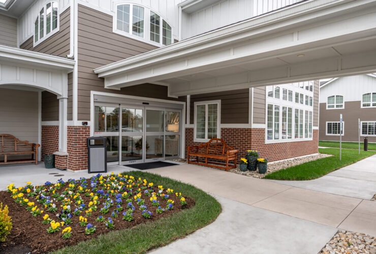 Welcoming entrance with benches, colorful flowers, and accessible walkways in a residential community setting.