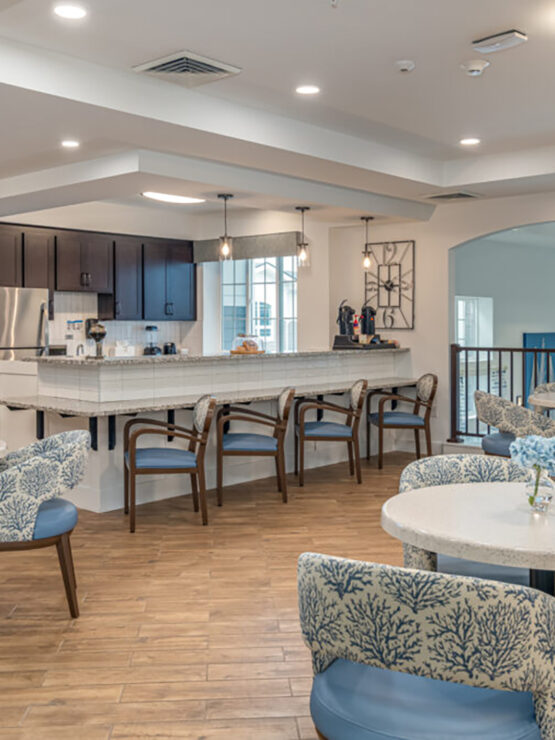 Bright, inviting communal dining area with seating and a fully equipped kitchen for resident gatherings.