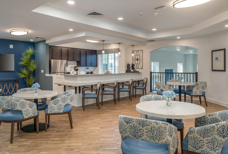 Bright, inviting communal dining area with seating and a fully equipped kitchen for resident gatherings.