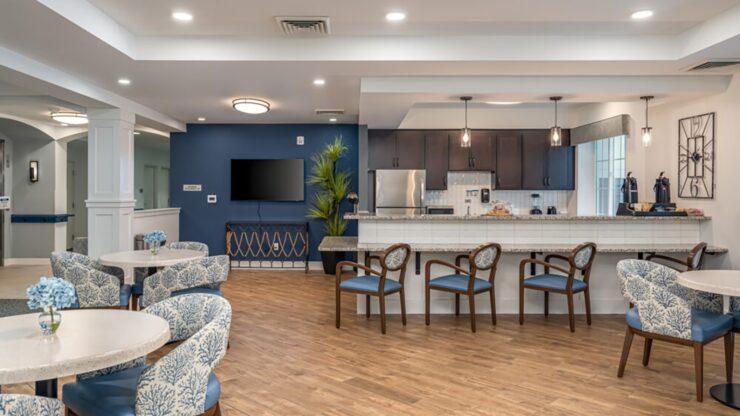 Open community room with comfortable seating, a kitchenette, and warm wood flooring.