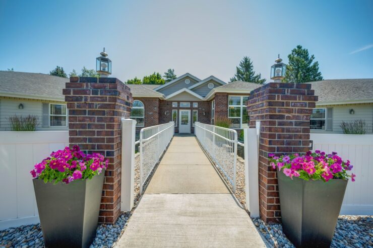 Welcoming walkway with vibrant flowers leading to a bright, inviting retirement community entrance.