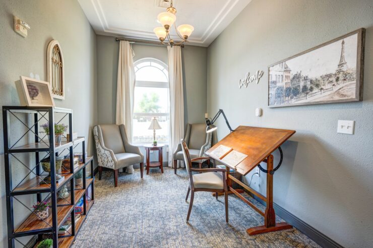 Well-lit sitting and activity room with comfortable chairs, art desk, and warm decor.