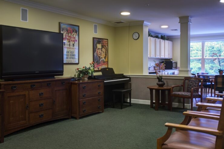 Activity room with piano, TV, comfortable seating, and natural light fostering community gatherings.