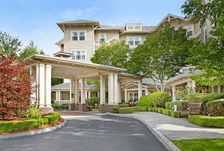 Elegant retirement community entrance surrounded by lush greenery and welcoming outdoor seating.