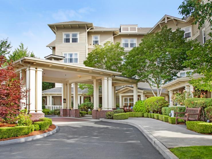 Elegant retirement community entrance surrounded by lush greenery and welcoming outdoor seating.