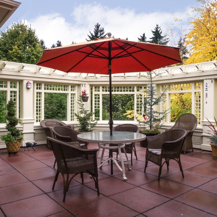 Outdoor seating area with umbrella, surrounded by greenery and comfortable chairs for gathering.