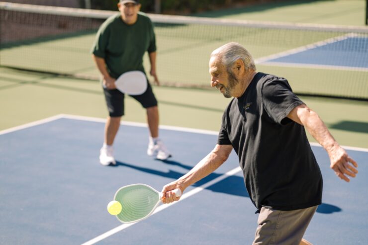 Two seniors enjoy an active game of pickleball on a sunny outdoor court.