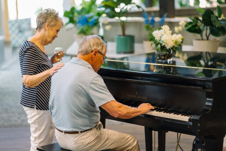 Senior couple enjoying music by the piano in a bright, plant-filled community space