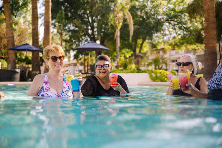 Seniors enjoying refreshing drinks and lively conversation together in a sunny pool setting.