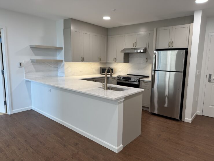 Modern kitchen with stainless steel appliances, bright countertops, and warm lighting.