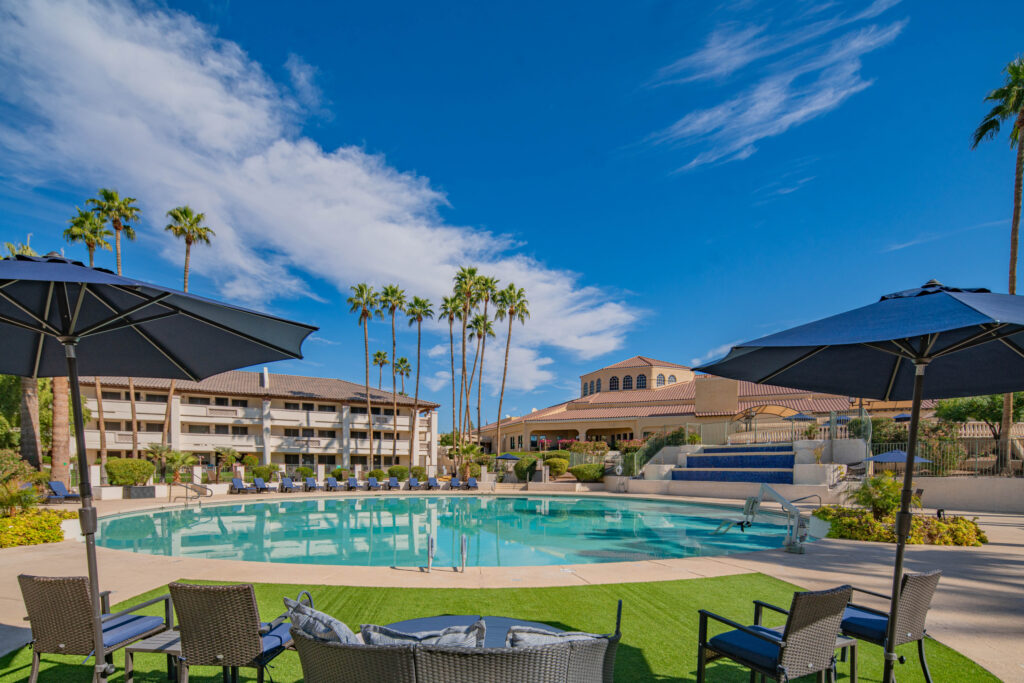 Sunlit pool area with comfortable seating, umbrellas, and palm trees in a welcoming community setting.