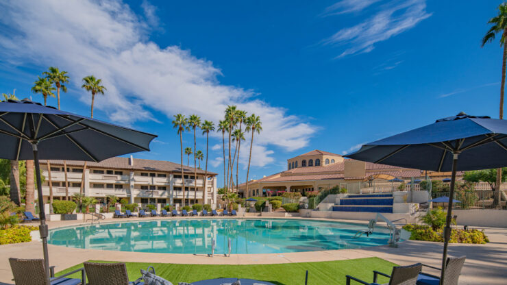 Sunlit pool area with comfortable seating, umbrellas, and palm trees in a welcoming community setting.