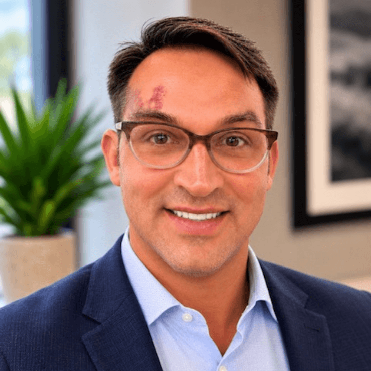 Professional man in glasses smiles warmly in a bright, welcoming office setting.