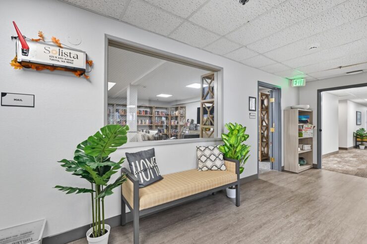 Welcoming seating area with plants and view into a bright, inviting common room filled with books.