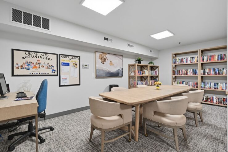 Well-lit community room with bookshelves, comfortable seating, and welcoming decor for residents.