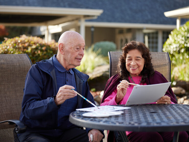 Two seniors enjoying painting together outdoors in a peaceful retirement community garden.
