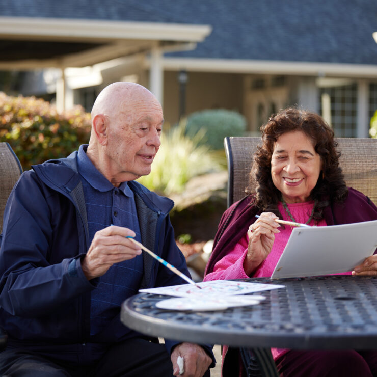 Two seniors enjoying painting together outdoors in a peaceful retirement community garden.