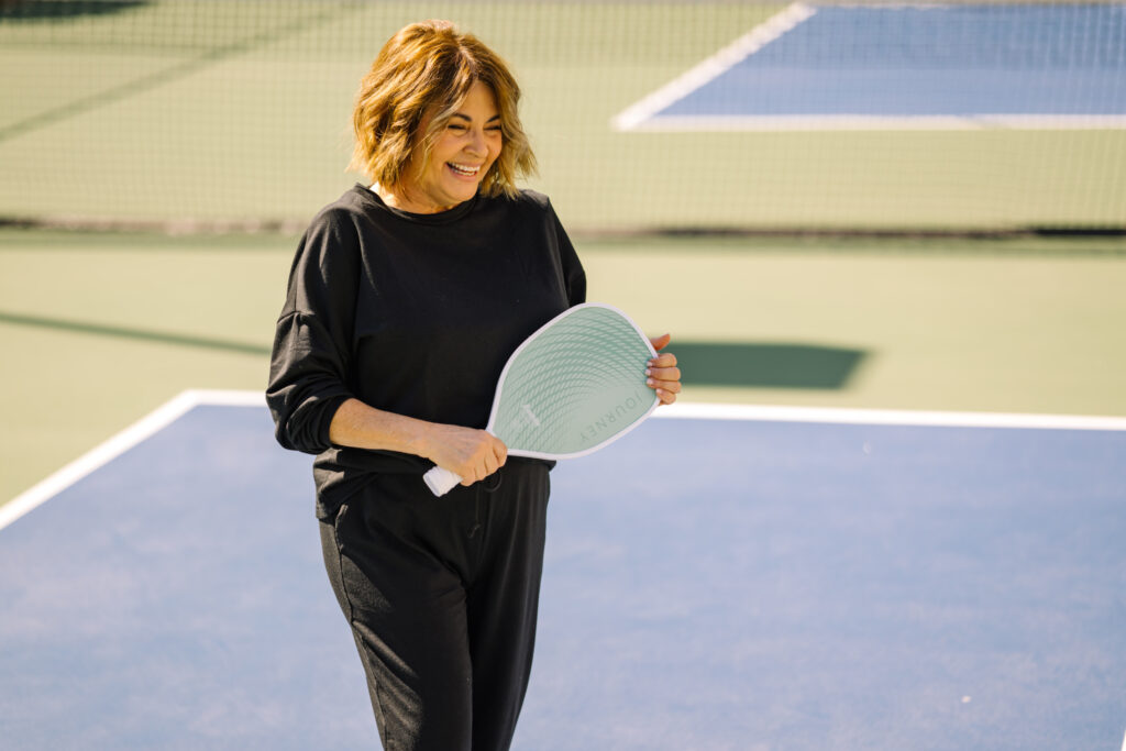 A smiling woman enjoying a sunny day playing pickleball on a community court.