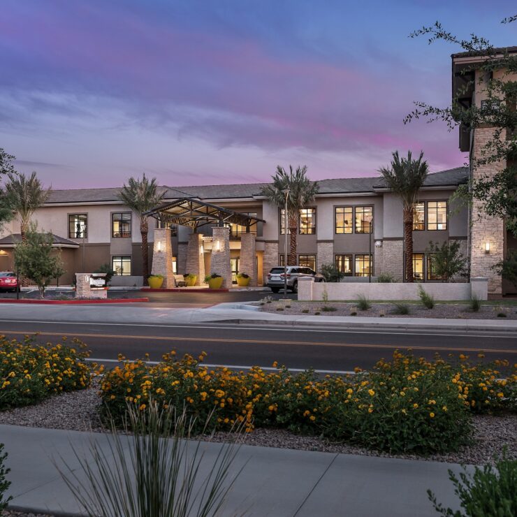 Well-lit entrance of a welcoming retirement community surrounded by landscaping at dusk.