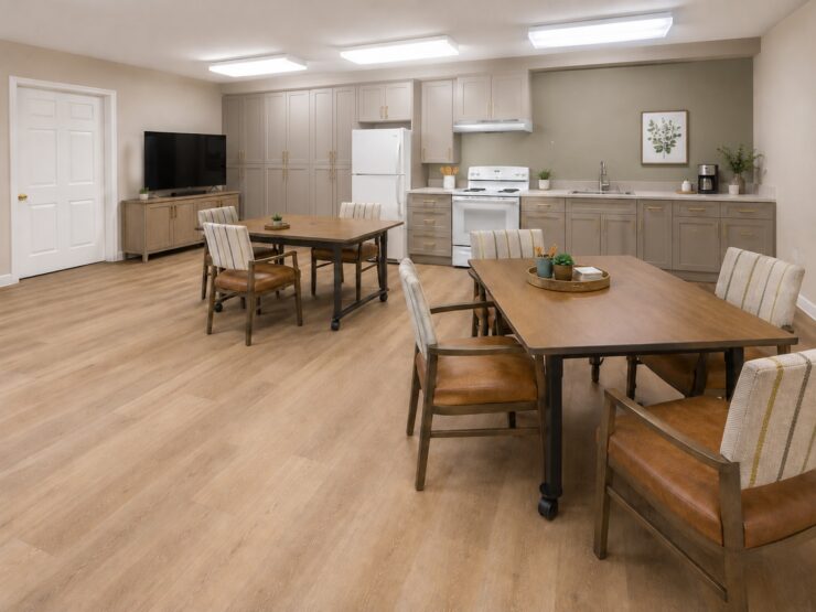 Bright activity room with dining tables, comfortable chairs, and a fully equipped kitchen.