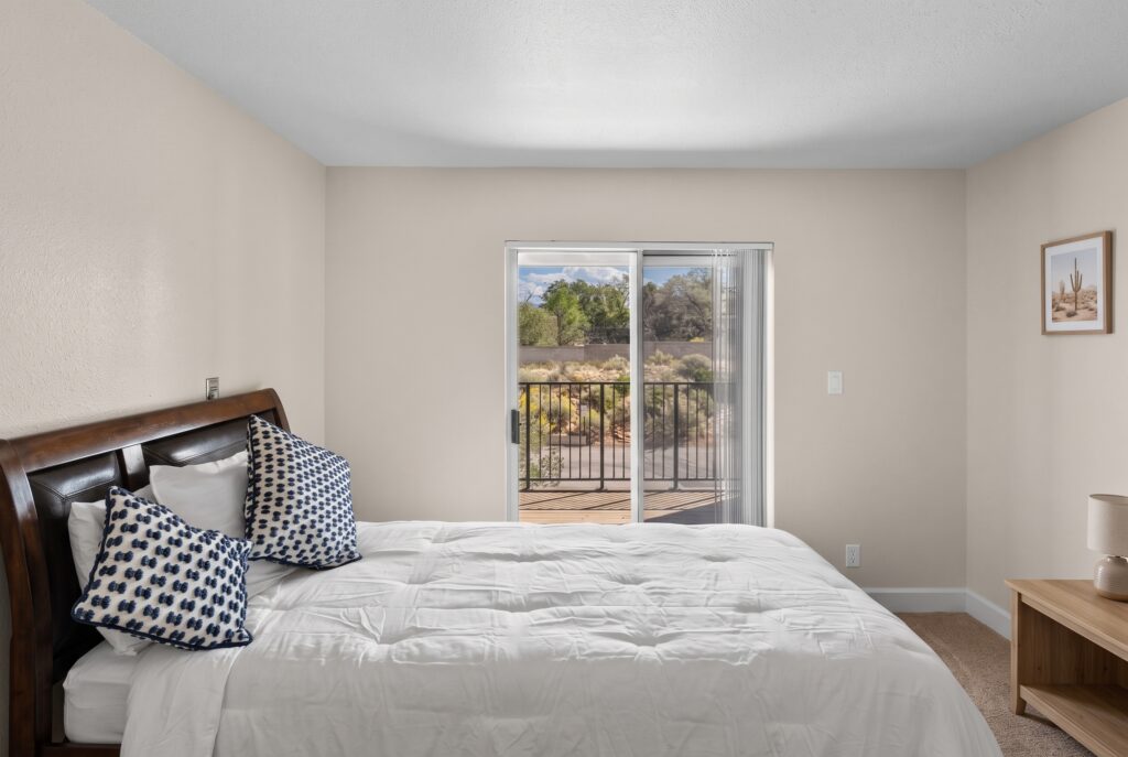Bright bedroom with soft bedding, decorative pillows, and a balcony overlooking greenery.