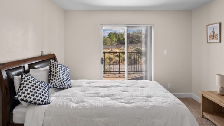 Bright bedroom with soft bedding, decorative pillows, and a balcony overlooking greenery.