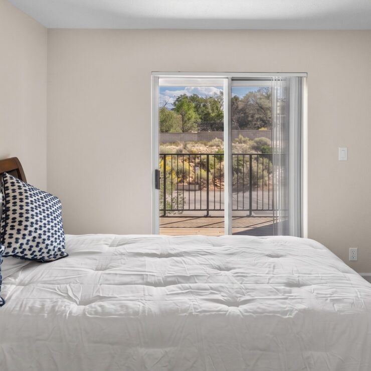 Bright bedroom with soft bedding, decorative pillows, and a balcony overlooking greenery.