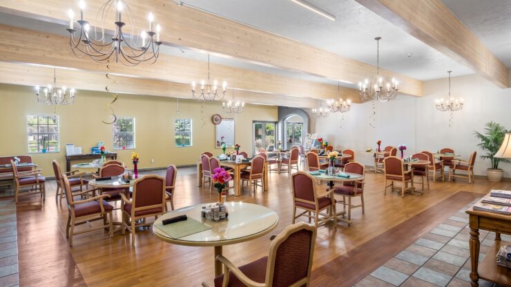 Spacious dining room with warm lighting, comfortable seating, and floral table accents fostering community.